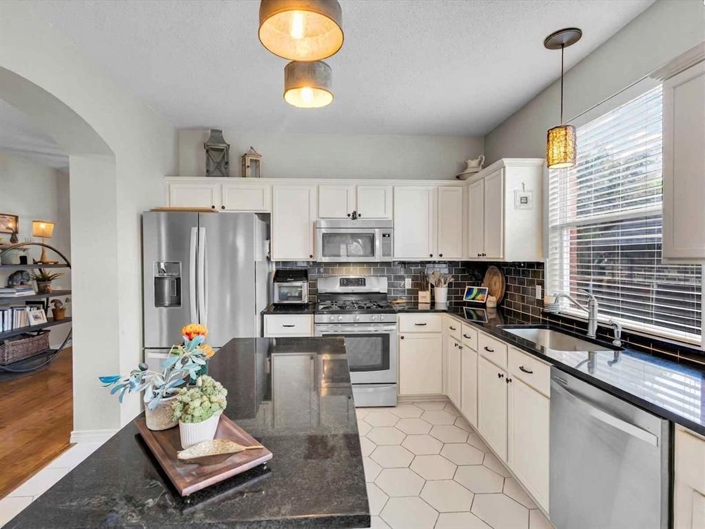 Kitchen featuring an island with a black countertop, white shaker-style cabinetry, stainless steel appliances, and a dark tile backsplash