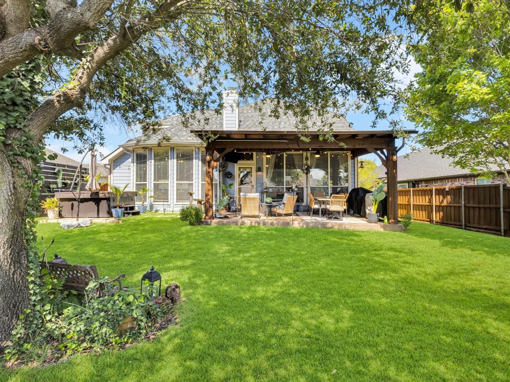 Expansive backyard featuring a manicured lawn, mature trees, and a wooden pergola covering a patio area