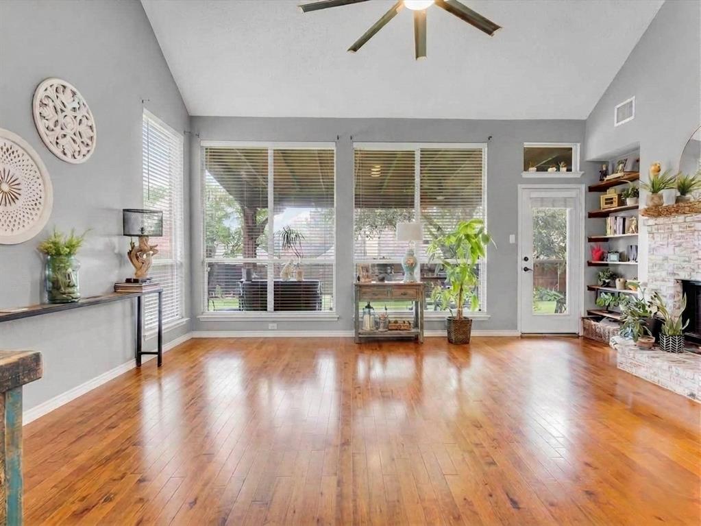 Vaulted ceilings, wood-finish flooring, full-light glass door, built-in corner shelving, and a stone-clad fireplace