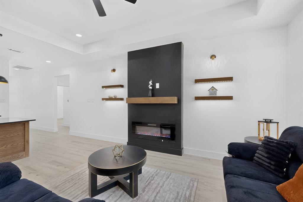 Modern living area featuring a fireplace with a black surround and wood mantel, recessed lighting, wood-finish flooring, and tray ceiling details