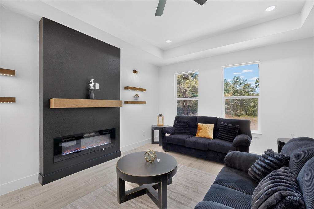 Living area featuring a modern black fireplace wall with a wood mantel, an electric firebox, and integrated floating shelves