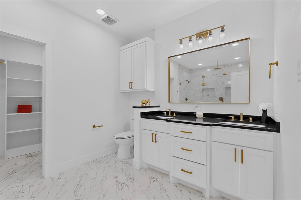 Bathroom featuring a dual vanity with black countertops, white cabinetry, and gold-finish hardware