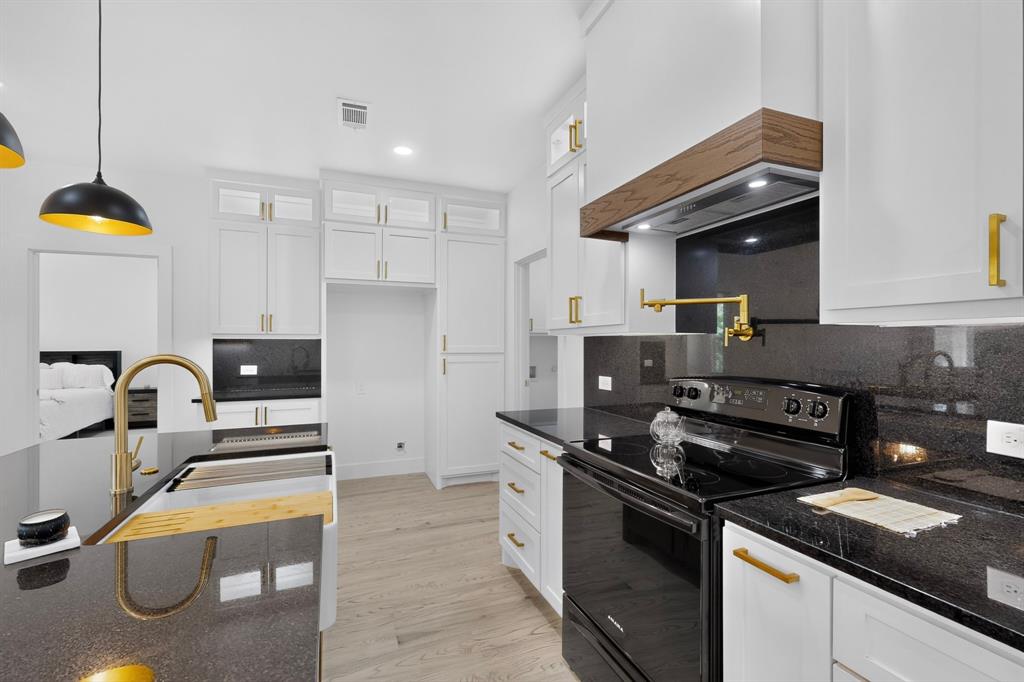 Contemporary kitchen featuring white cabinetry with gold-tone hardware, dark countertops, and light wood-finish flooring