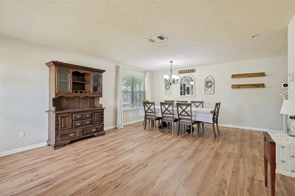 Spacious room featuring wood-finish flooring, a contemporary chandelier, large window with blinds, and white baseboards