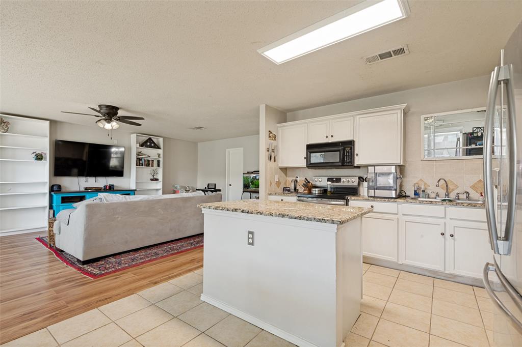 Open-concept kitchen and living area featuring a central kitchen island with a stone-finish countertop, white cabinetry, a stainless steel refrigerator, and tiled flooring