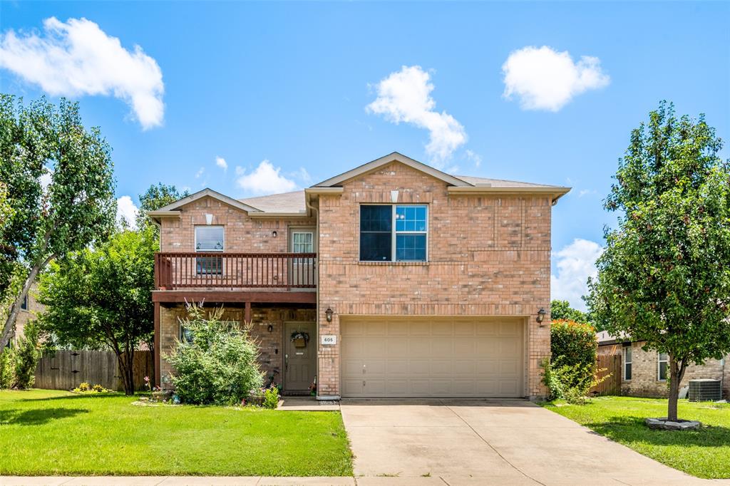 Two-story brick exterior featuring a second-level balcony with wood railing, a two-car garage, and a concrete driveway