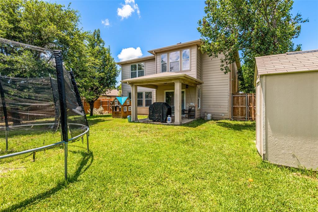 Expansive grassy backyard featuring a covered patio, a detached storage shed, mature trees, and privacy fencing
