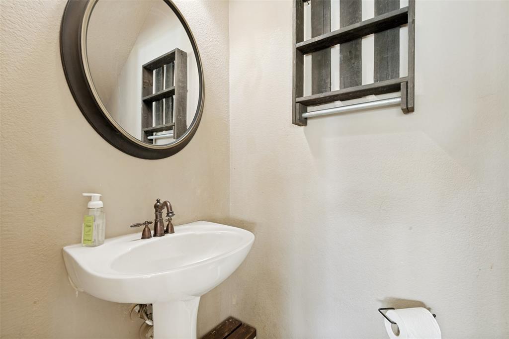 Pedestal sink featuring a bronze-finish faucet, circular framed mirror, and a wall-mounted wooden shelf unit with a towel bar
