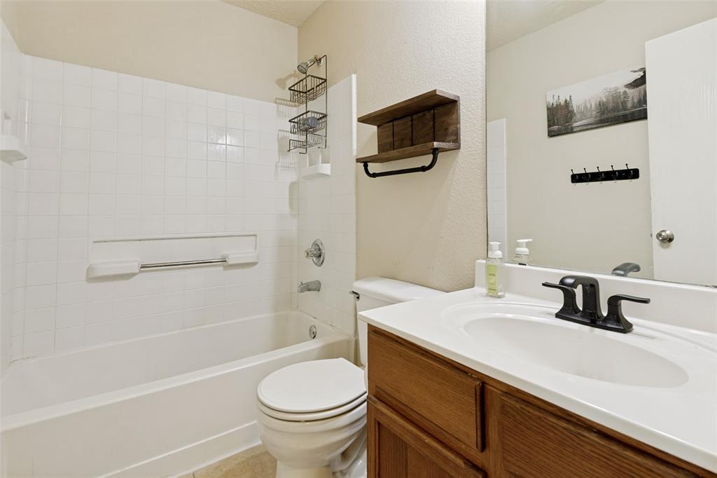 Full bathroom featuring a white ceramic bathtub with tiled surround, a white toilet, and a vanity with a white countertop and wood-finish cabinetry