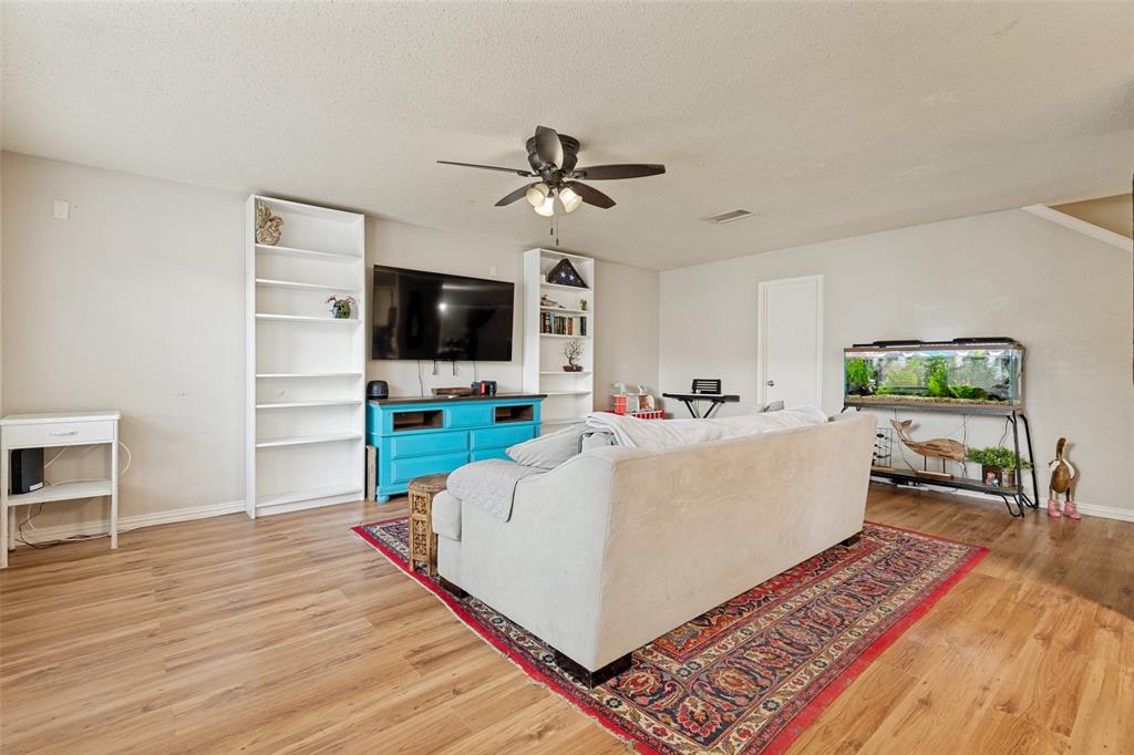 Living area featuring wood-finish flooring, light neutral wall paint, and a ceiling fan with integrated lighting