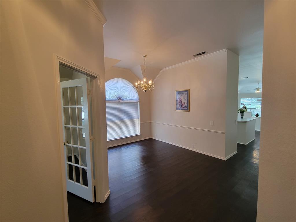 Entryway looking at dining room with chandelier, dark wood-style flooring, vaulted ceiling, and ornamental molding