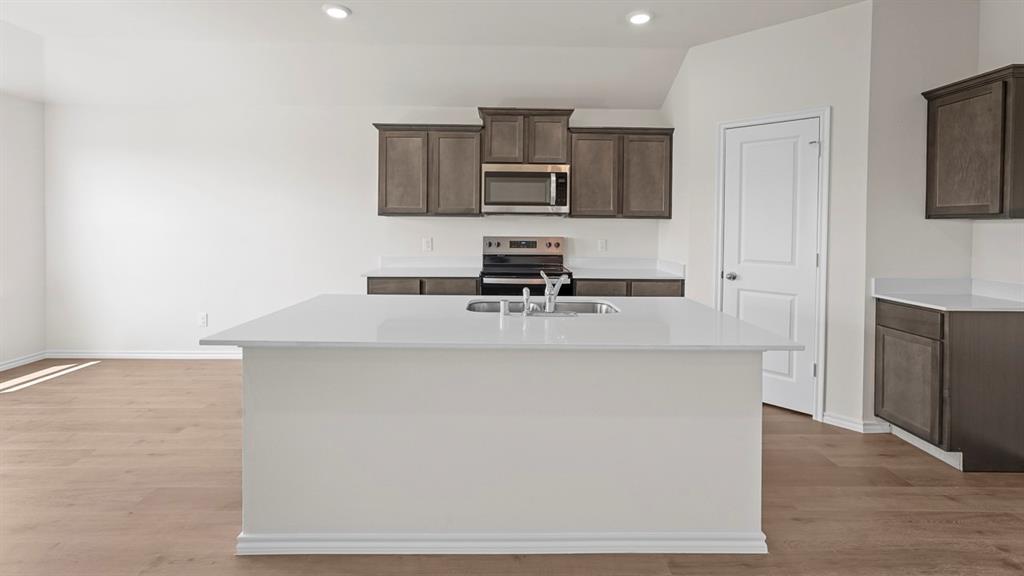 Kitchen featuring a white island with a double basin sink, stainless steel appliances, dark wood-finish cabinetry, white countertops, and wood-finish flooring
