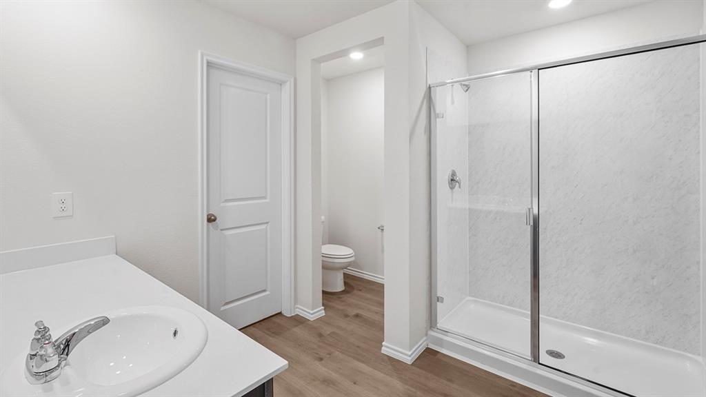 Bathroom featuring a glass-enclosed shower with white paneling, a white vanity with an integrated sink, chrome faucet, and wood-finish flooring