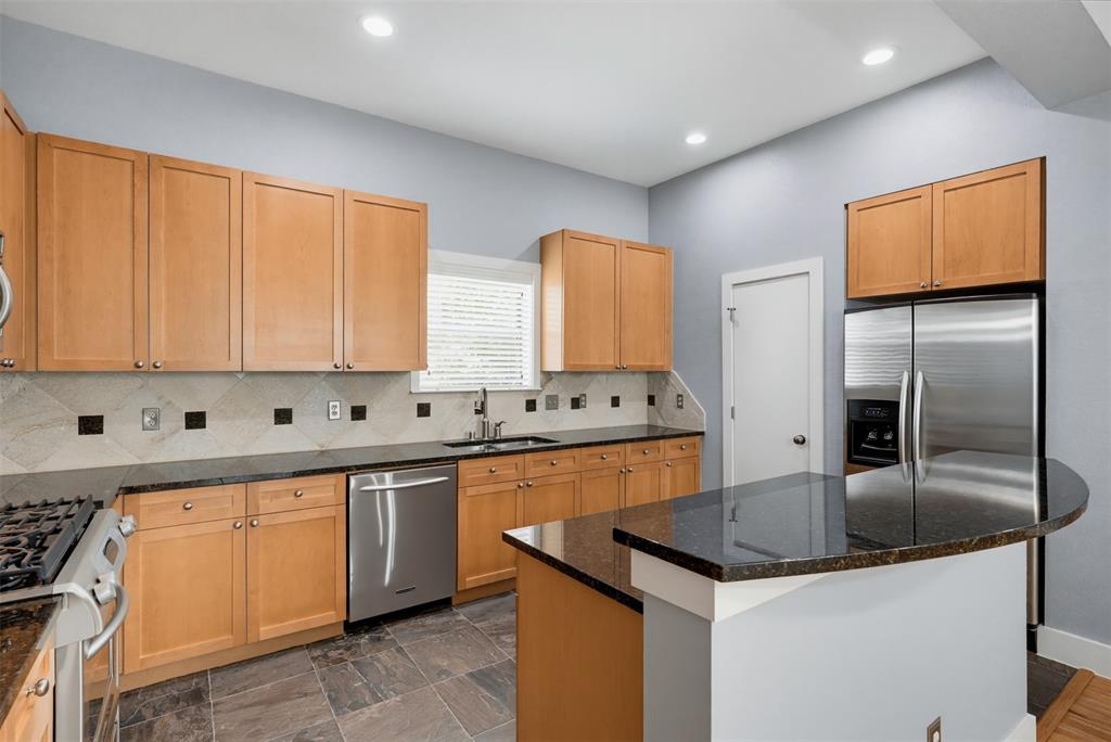 Kitchen featuring light wood cabinetry, granite countertops, stainless steel appliances, a tiled backsplash with accent squares, and slate-finish floor tiles
