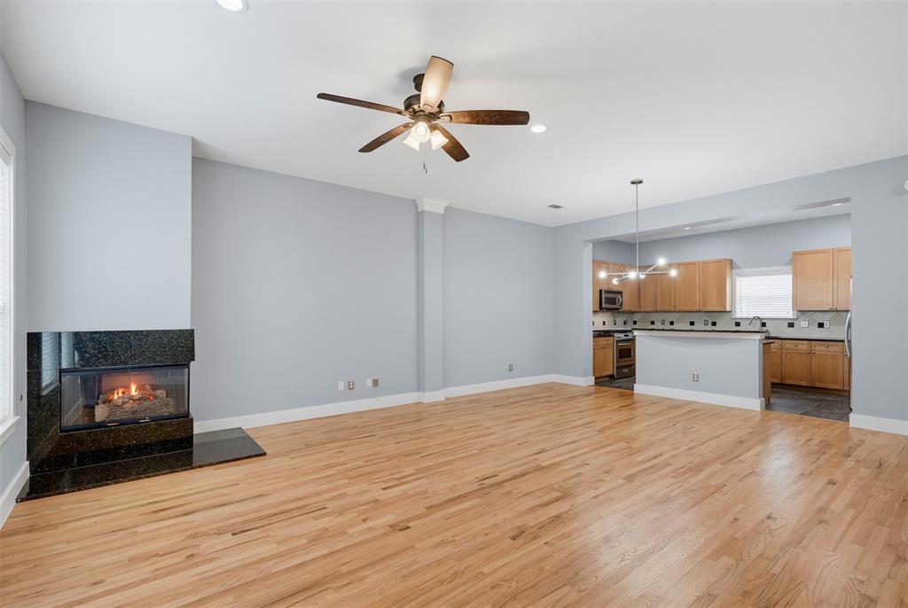 Open-concept living area featuring wood-finish flooring, a contemporary fireplace with a dark stone surround, and recessed lighting