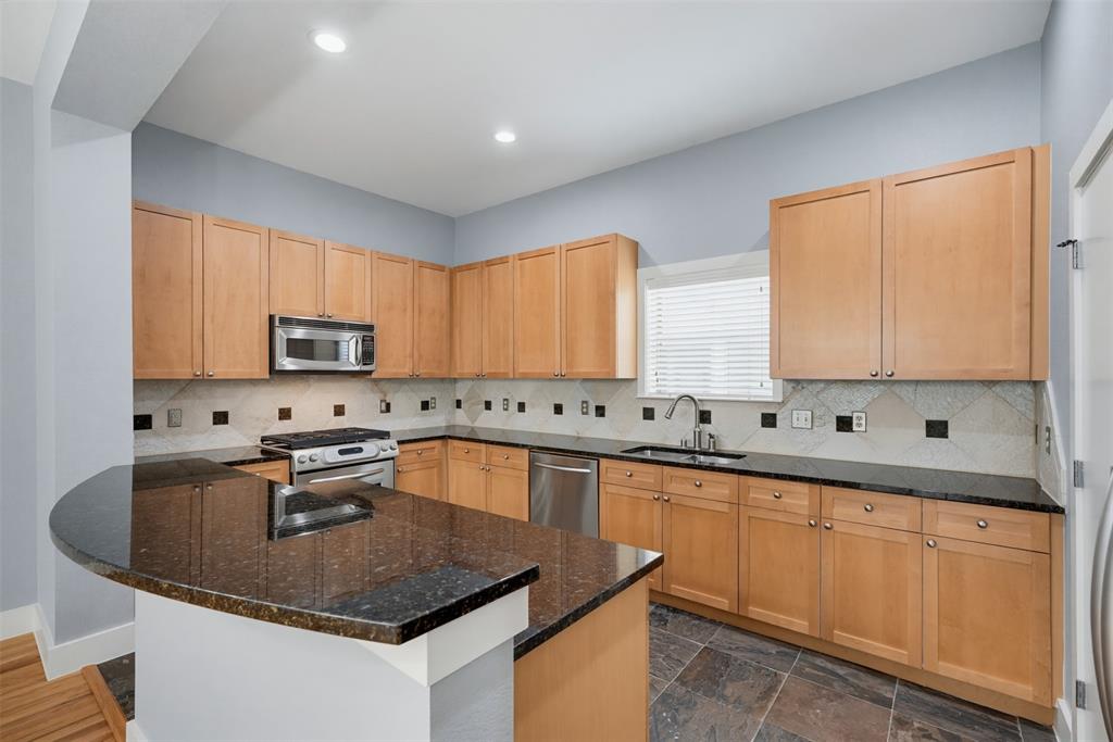 Kitchen featuring a curved peninsula with a dark countertop, light wood cabinetry, a stainless steel microwave, a stainless steel range, and a stainless steel dishwasher