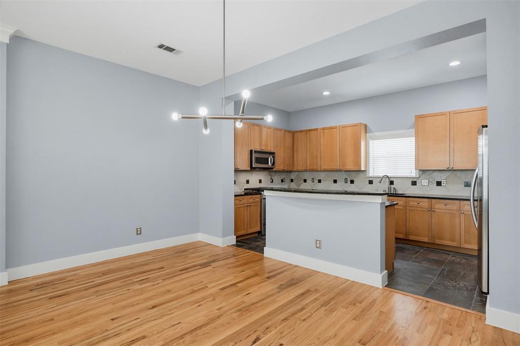 Open-concept living area featuring wood-finish flooring, a contemporary linear chandelier, and a kitchen with wood cabinetry, stainless steel appliances, and a tiled backsplash