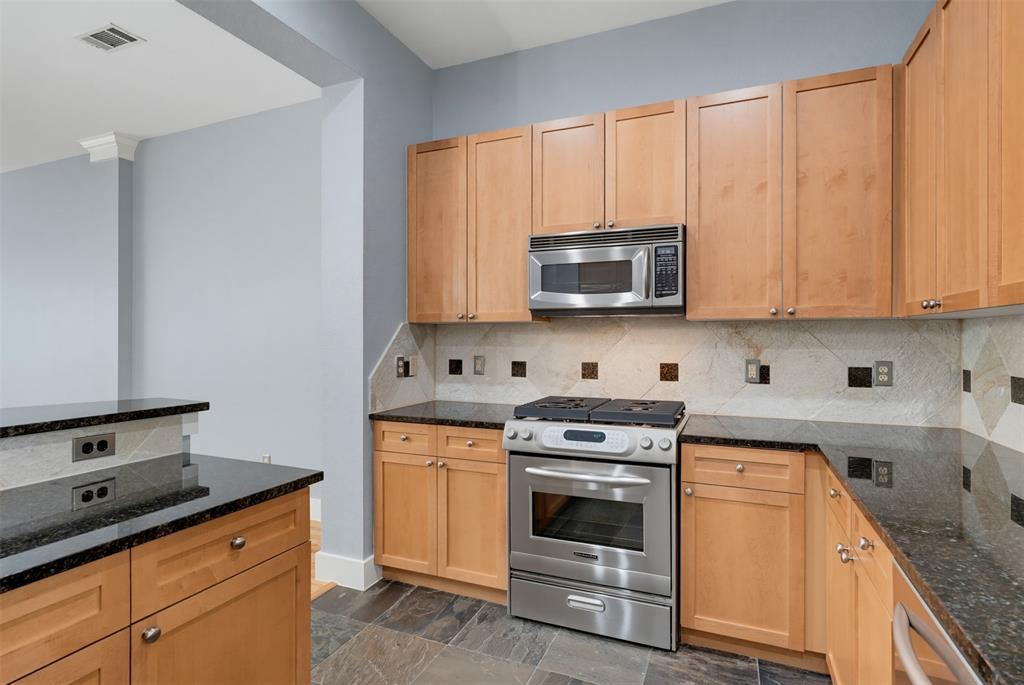 Kitchen featuring wood-finish cabinetry, black stone countertops, stainless steel appliances, and a decorative tile backsplash
