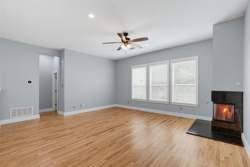 Spacious room featuring wood-finish flooring, a contemporary fireplace with a dark stone surround and hearth, and three large windows