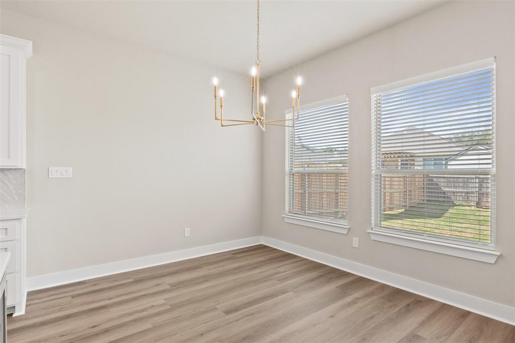 Dining area featuring wood-finish flooring, a modern gold-tone chandelier, two windows with blinds, and light-toned walls Dining area featuring wood-finish flooring, a modern gold-tone chandelier, two windows with blinds, and light-toned walls