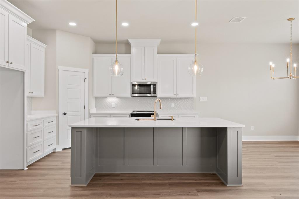 Modern kitchen featuring a spacious gray island with a white countertop, white cabinetry, brass pendant lighting, and wood-finish flooring Modern kitchen featuring a spacious gray island with a white countertop, white cabinetry, brass pendant lighting, and wood-finish flooring