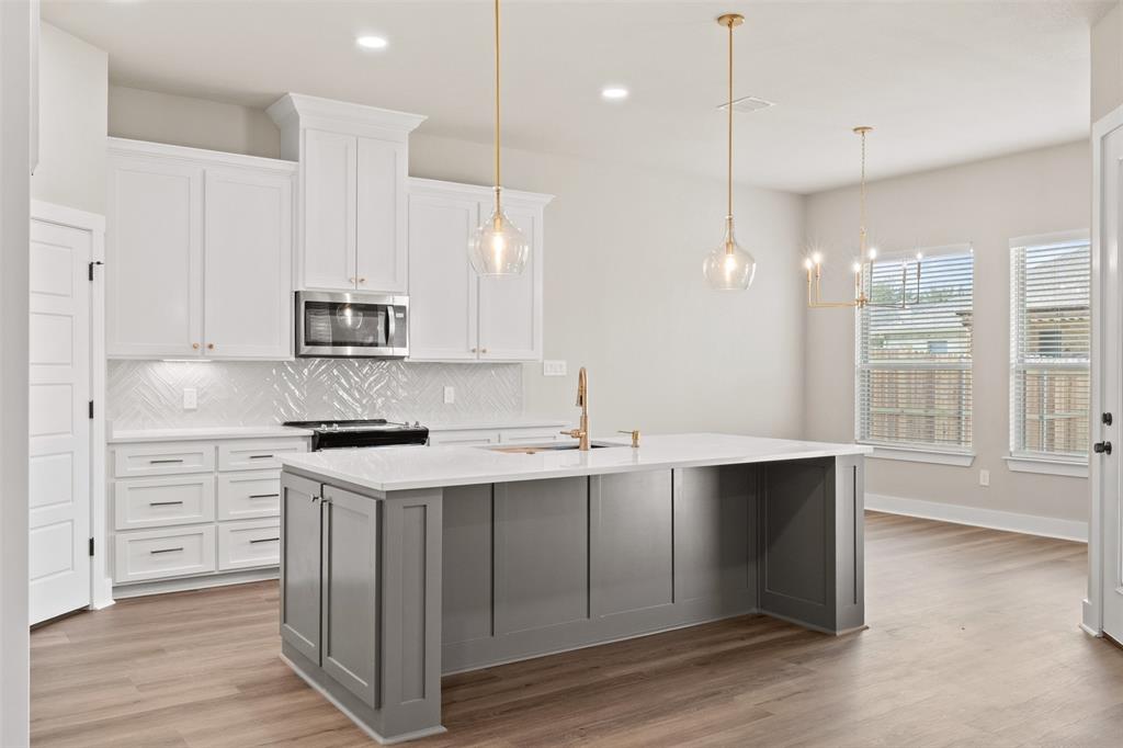 Modern kitchen featuring a large central island with a light-colored countertop, white shaker-style cabinetry, and wood-finish flooring Modern kitchen featuring a large central island with a light-colored countertop, white shaker-style cabinetry, and wood-finish flooring