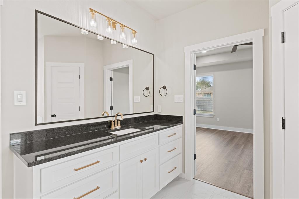Bathroom vanity featuring a large mirror with a black frame, a dark stone countertop, and a white cabinet with gold-toned hardware