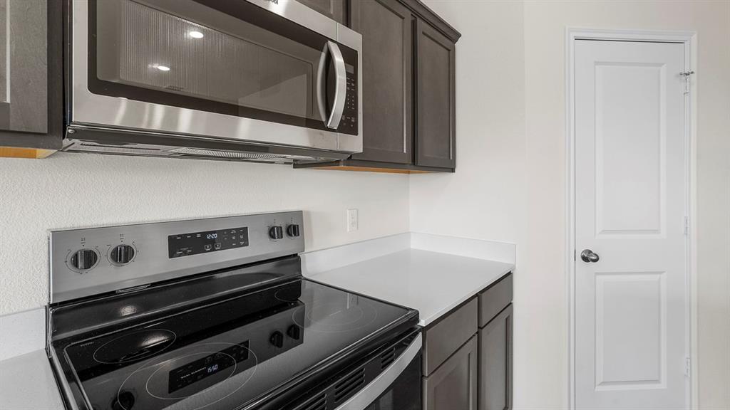Modern kitchen featuring a stainless steel microwave, electric range with a ceramic cooktop, dark wood-finish cabinetry, and light-toned countertops
