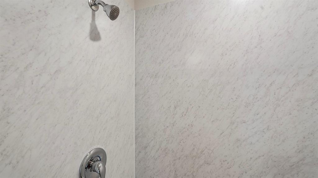Shower enclosure featuring textured wall panels and polished chrome fixtures