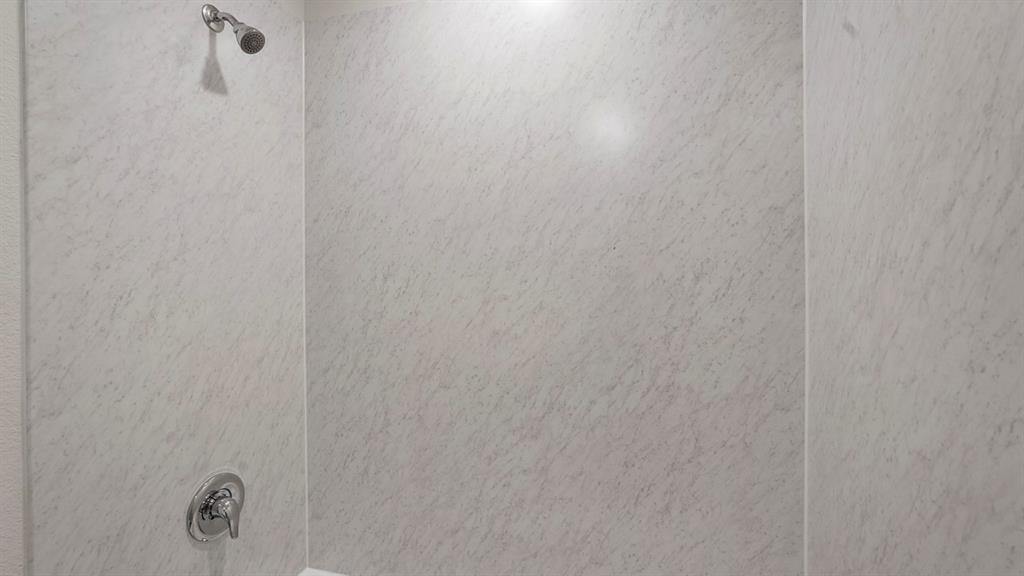 Shower stall featuring light-toned, textured wall panels and chrome fixtures