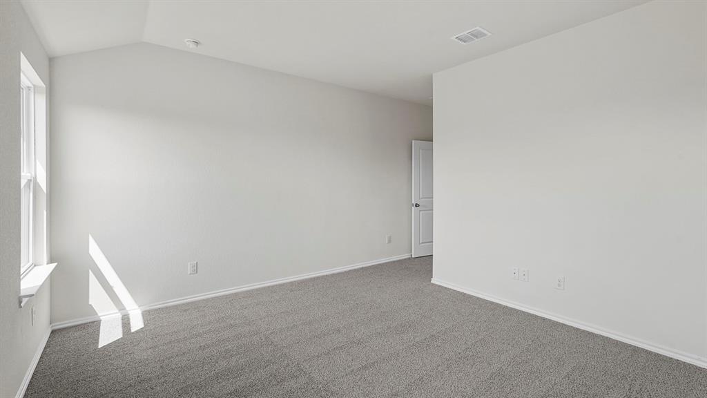 Spacious room featuring vaulted ceilings, a large window, neutral wall paint, gray carpet flooring, and a white six-panel door