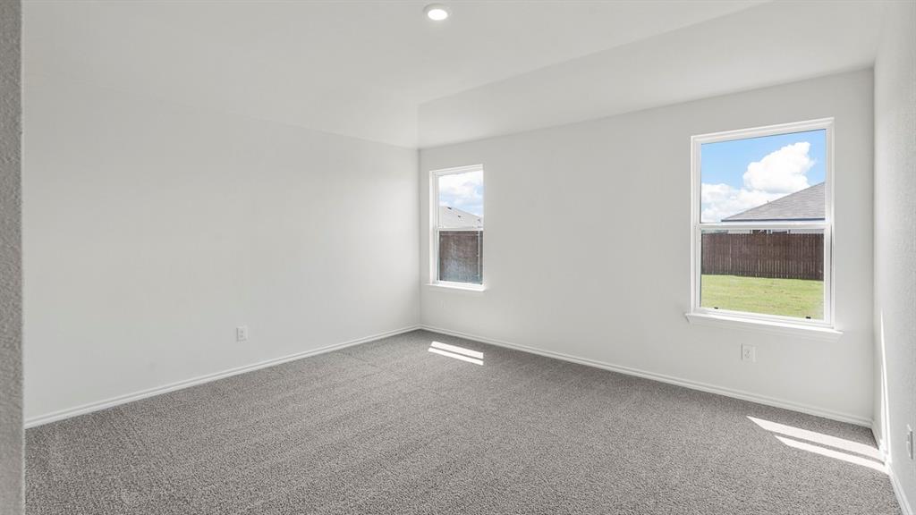 Spacious room featuring light gray carpeting, neutral wall finishes, and two windows providing natural illumination