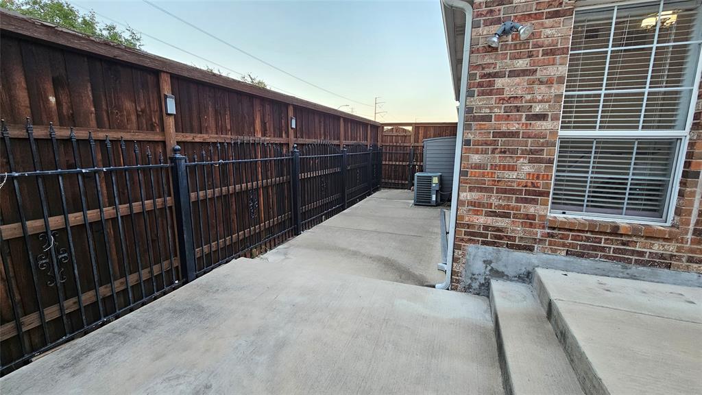 Concrete patio area featuring a brick exterior wall, a window with horizontal blinds, and a durable wood privacy fence with decorative wrought iron accents