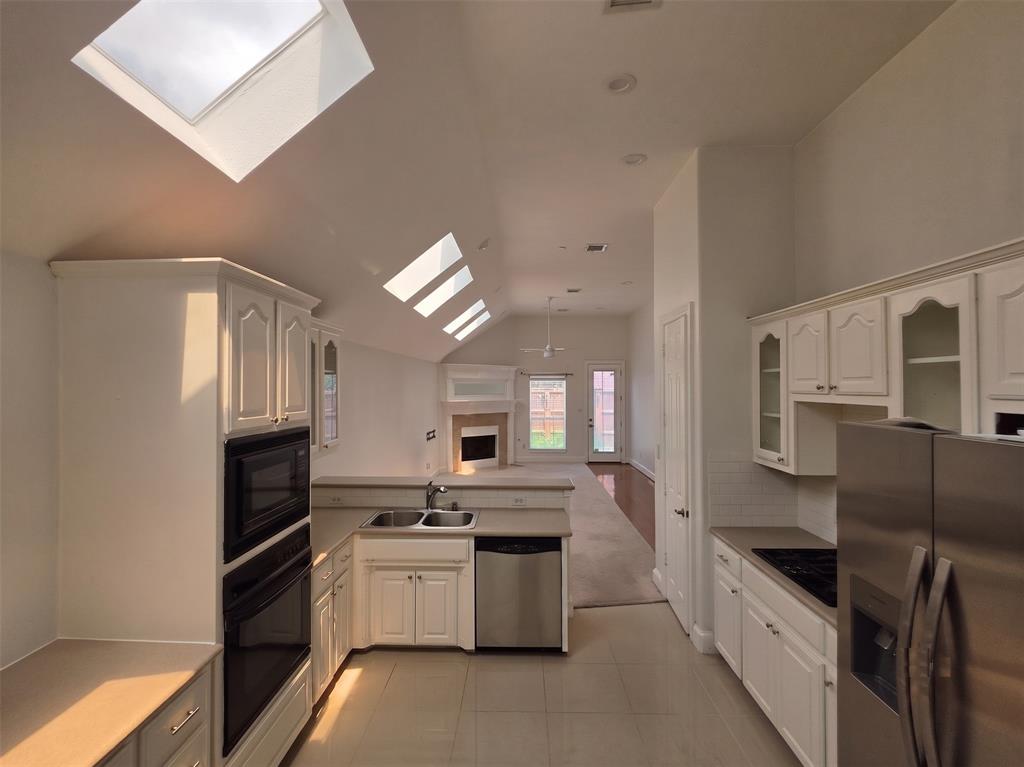 Kitchen featuring white cabinetry with glass inserts, dual stainless steel sink, integrated stainless steel appliances, and tile flooring