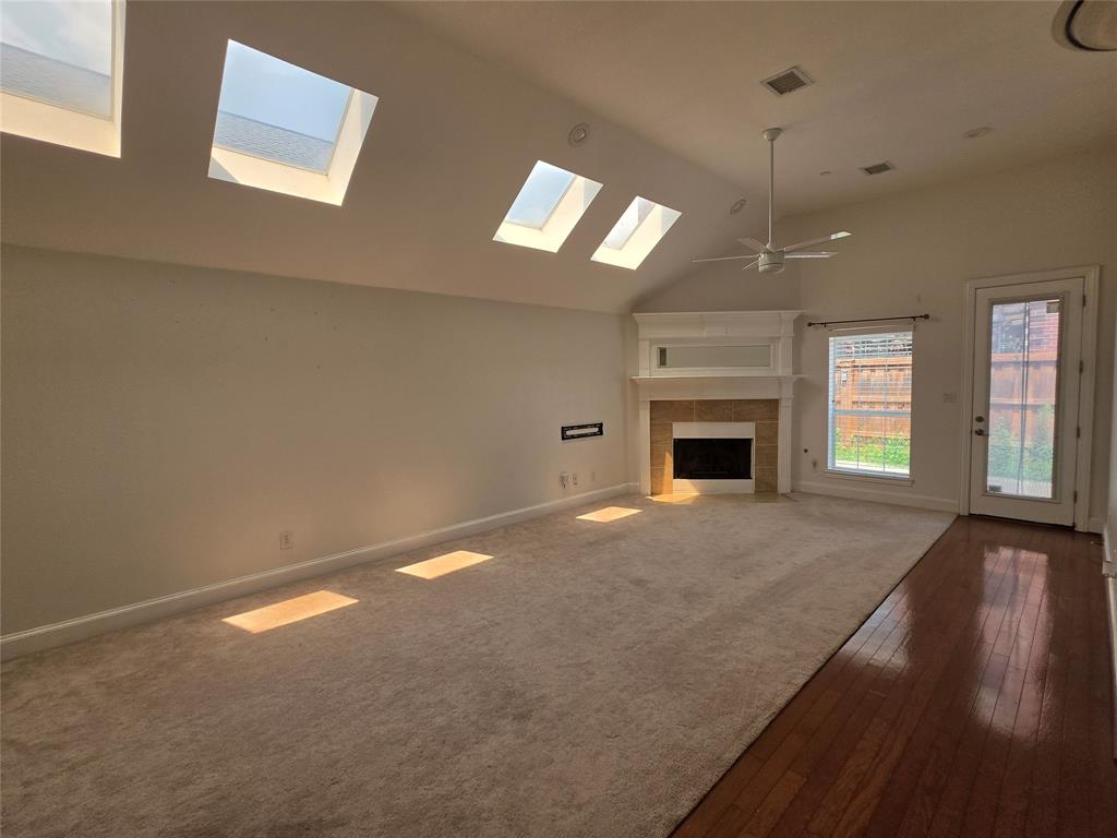 Spacious interior featuring a vaulted ceiling with multiple skylights, a fireplace with a mantel, a ceiling fan, and mixed flooring with carpet and wood-finish