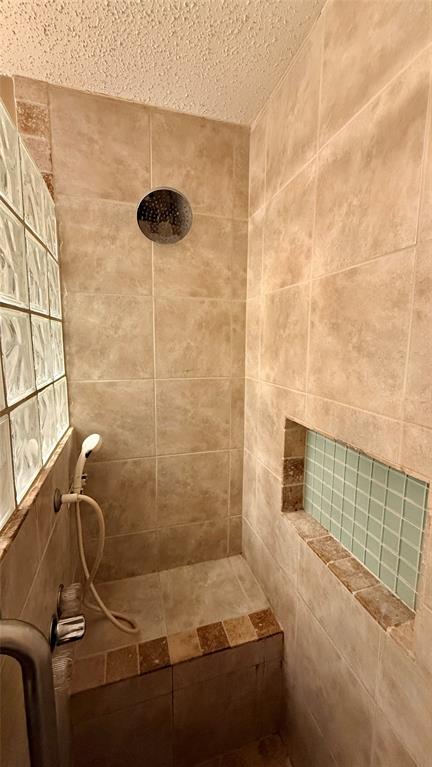 Tiled shower enclosure featuring a built-in bench, recessed niche with mosaic tile, glass block wall, and a rainfall showerhead with a handheld sprayer