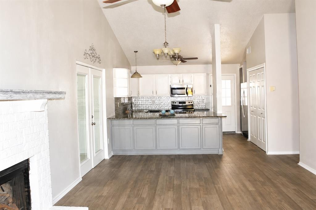 Spacious interior featuring wood-finish flooring, a white brick fireplace, vaulted ceilings, and white French doors