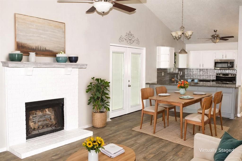 Virtually staged, vaulted ceiling, wood-finish flooring, white brick fireplace, glass-panel French doors, and a kitchen with white cabinetry and a backsplash