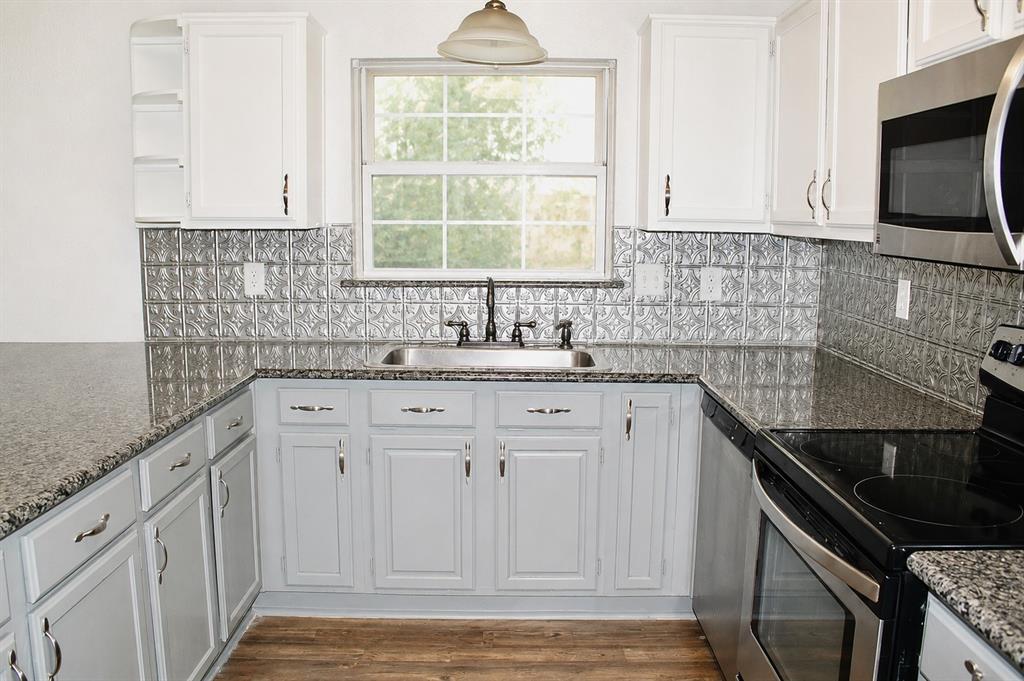 U-shaped kitchen featuring granite-look countertops, stainless steel appliances, a tin-look backsplash, and wood-finish flooring