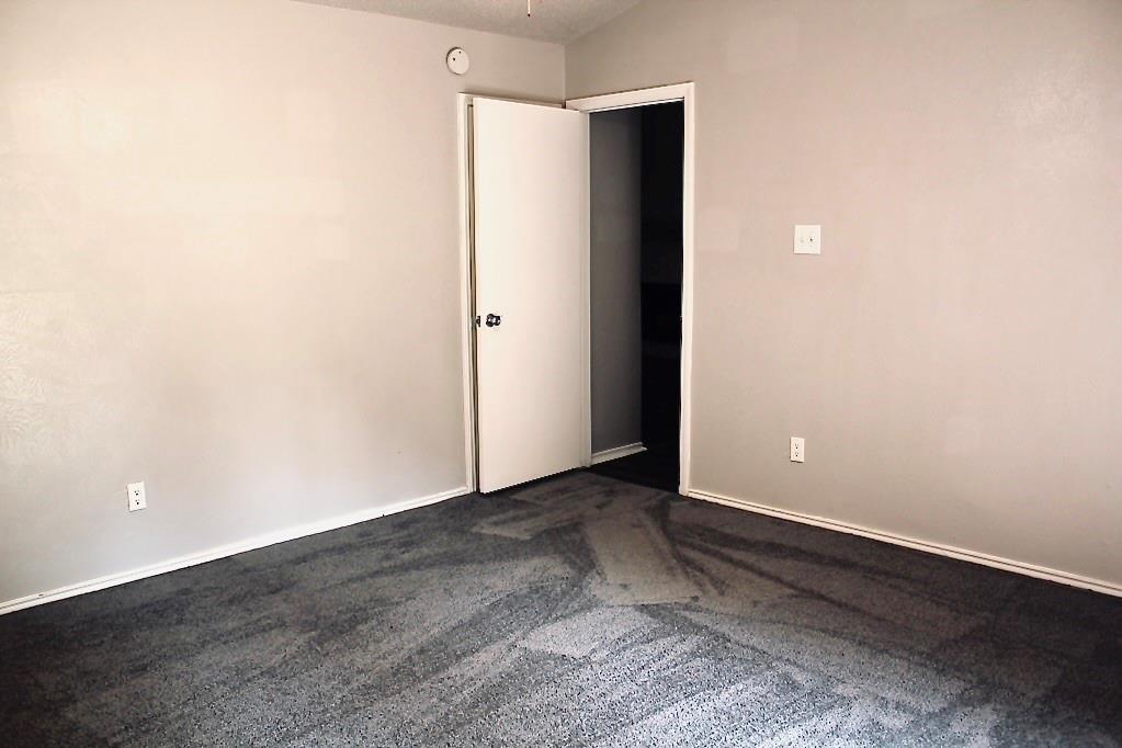 Light gray wall finishes with white trim, dark gray carpet, white interior door with black hardware, and a ceiling-mounted fixture