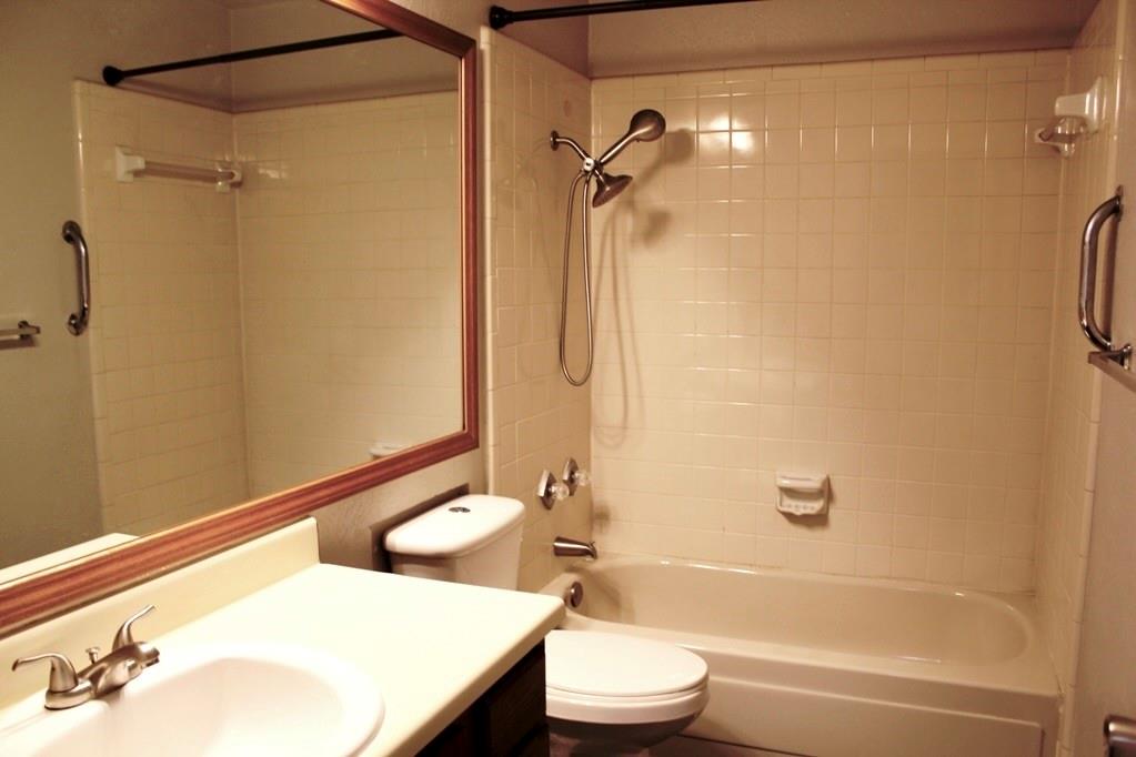 Built-in bathtub with subway tile surround, chrome shower fixtures, vanity with integrated sink, and framed wall mirror