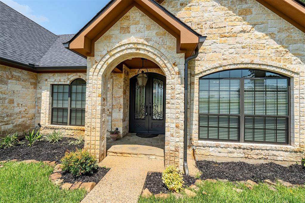 Stone facade entry featuring an arched doorway with iron double doors, an overhead pendant light fixture, and arched windows with horizontal blinds