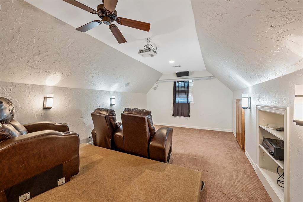 Carpeted entertainment space featuring sloped ceilings, ceiling fan, wall sconces, projector, and built-in shelving