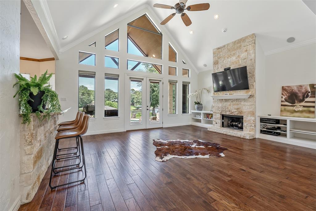 Living area featuring an expansive vaulted ceiling with exposed beams, wood-finish flooring, a stone-clad fireplace, and built-in shelving