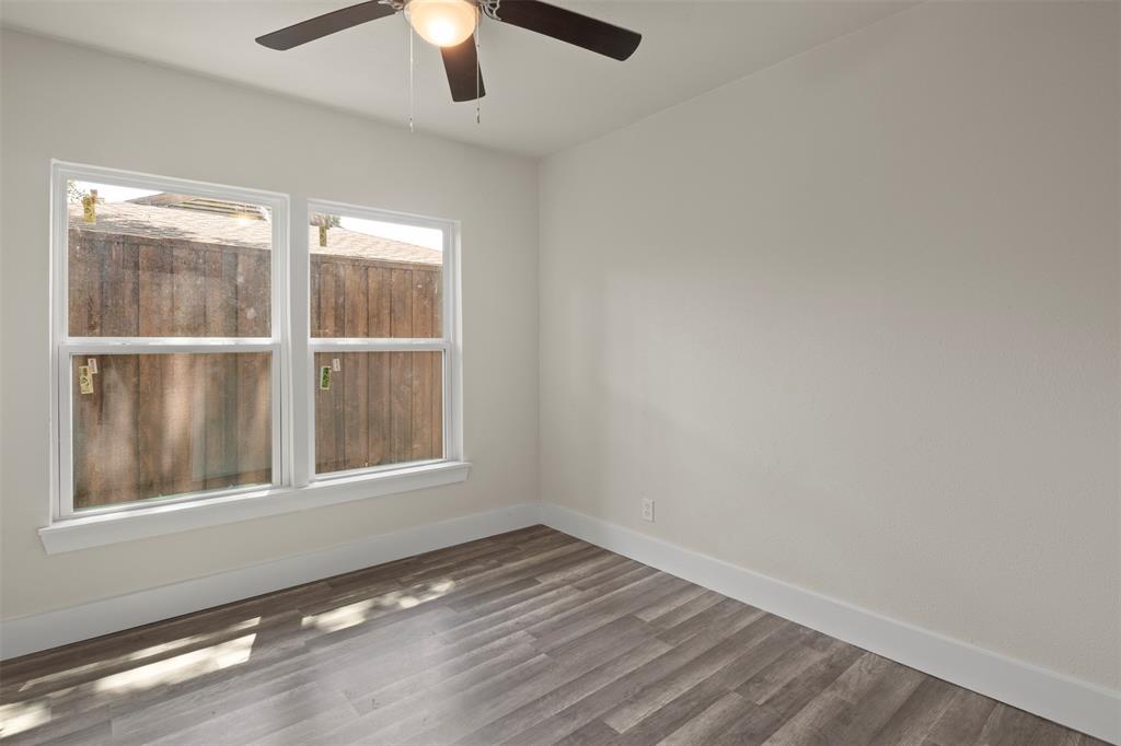 Bright room featuring two windows, wood-finish flooring, a ceiling fan with integrated lighting, and white baseboards
