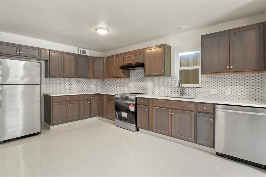 Kitchen featuring stainless steel appliances, dark wood-finish cabinetry, white countertops, a hexagonal tile backsplash, and light tile flooring