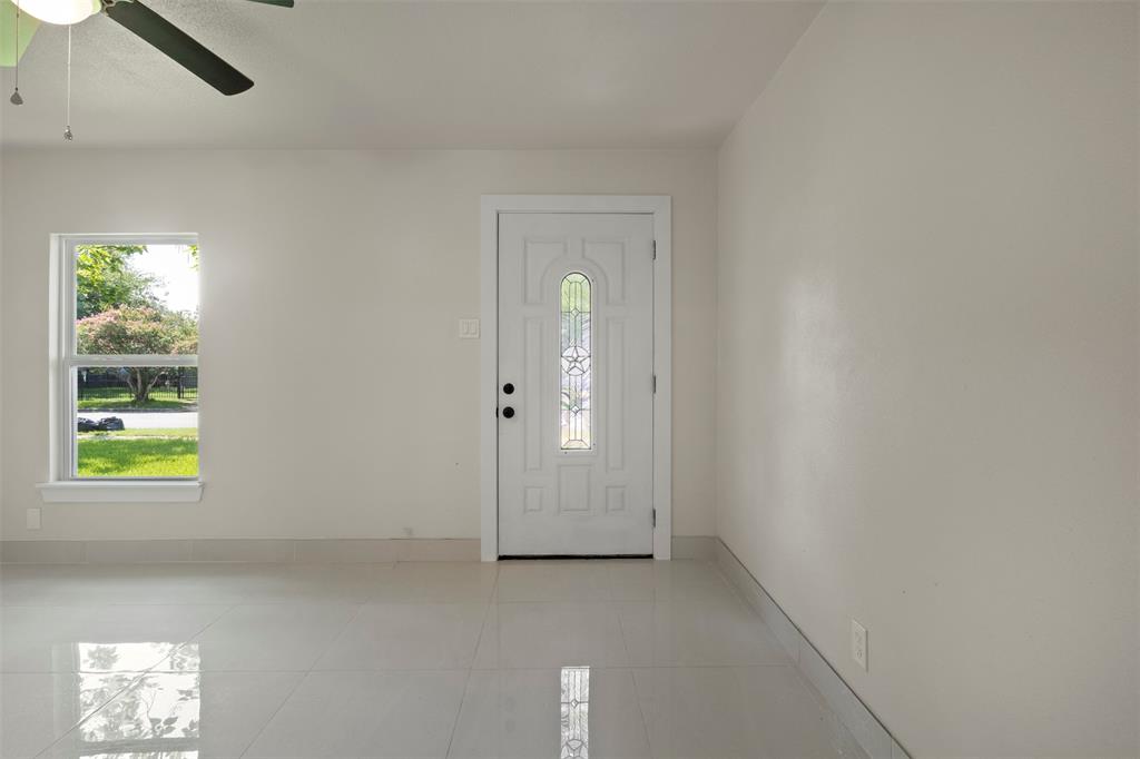 Entryway featuring a white door with decorative glass inserts, a single-pane window, light-colored walls, and glossy tile flooring