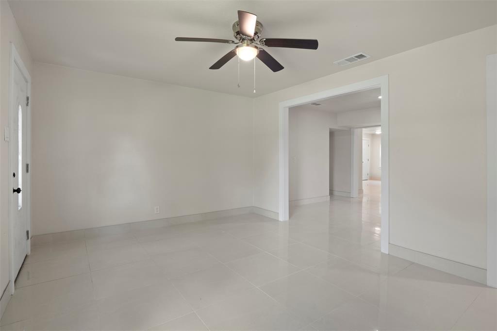 Expansive living area featuring light-toned tile flooring, neutral wall paint, and a ceiling fan with integrated lighting