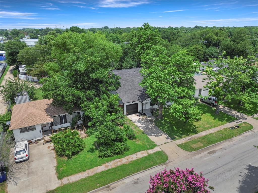 Residential property featuring a dark shingle roof, mature trees, and a concrete driveway
