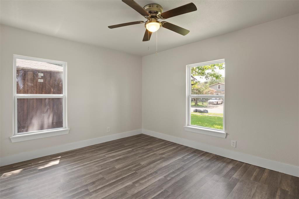 Open room featuring wood-finish flooring, two windows with white trim, and a ceiling fan with integrated lighting